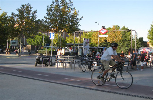 Ciclista en carril bici frente a una boca de Metro